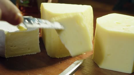 gouda, brie and swiss cheese on cutting board sliced with small knife