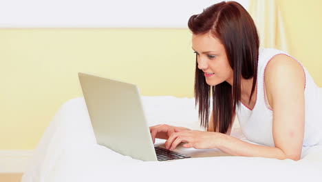 Pretty-brunette-lying-on-bed-using-her-laptop