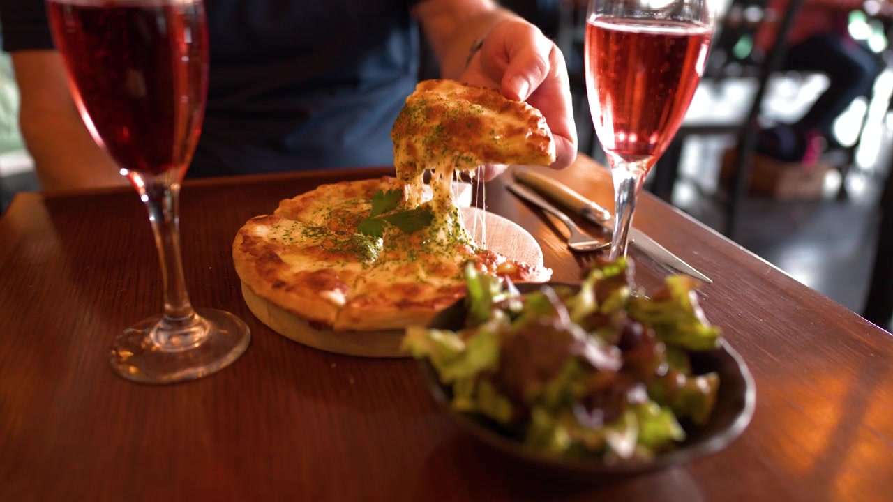 A hand lifts a slice of hot pizza with melting cheese at a restaurant table.