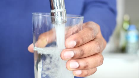 person filling a glass with water from a kitchen tap