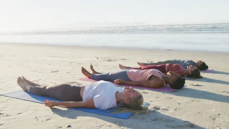 grupo de diversas amigas practicando yoga, acostadas en esteras en la playa