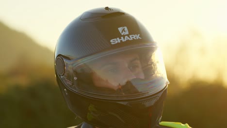 motorcyclist wearing a helmet stands outside at sunset, with cars visible in the background, close up shot in slowmotion
