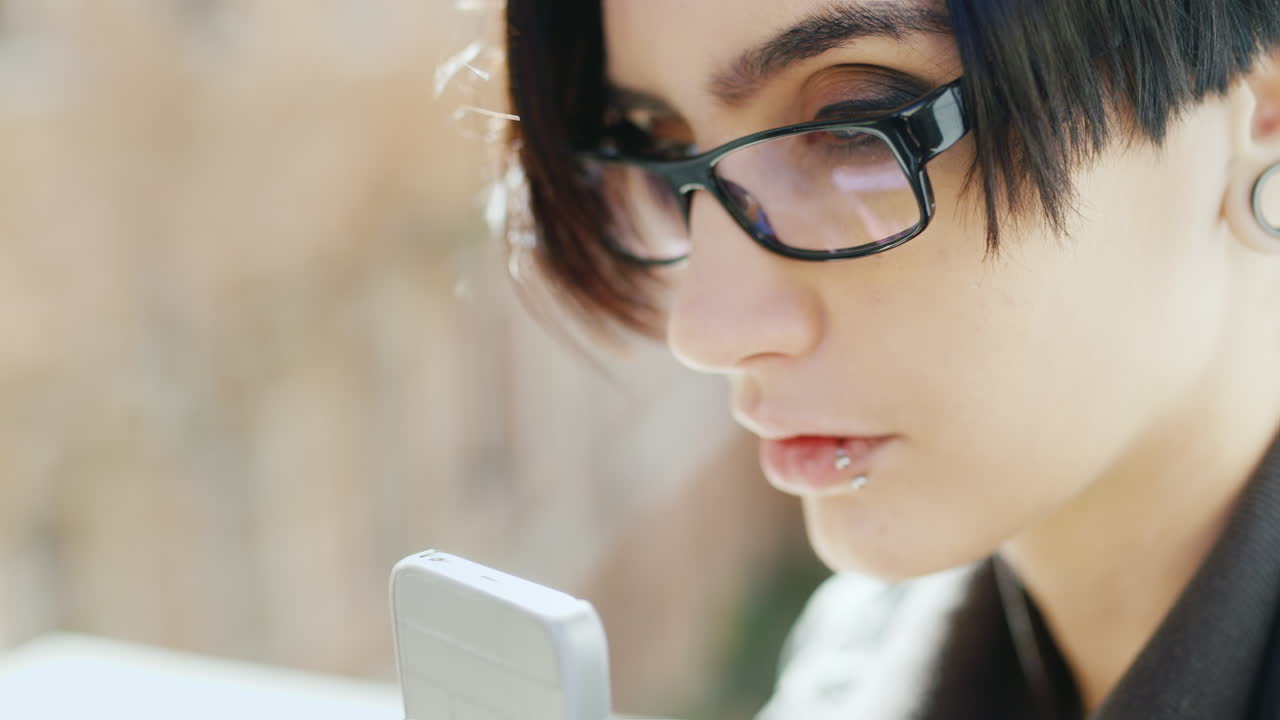 el primer plano de una morena atractiva con gafas hipster está escribiendo en un teléfono móvil sus manos con el ph