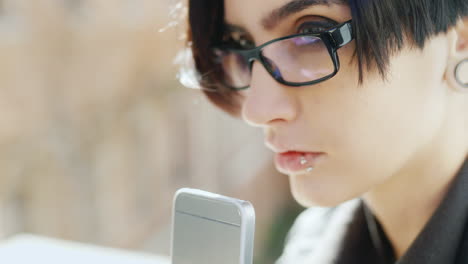Close-Up-Of-Attractive-Brunette-In-Hipster-Glasses-Is-Typing-On-A-Mobile-Teléfono-Her-Hands-With-The-Ph