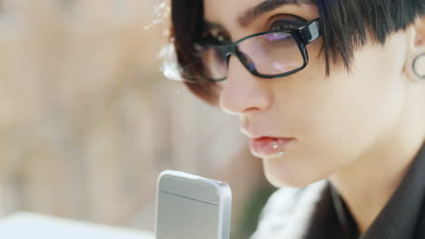 el primer plano de una morena atractiva con gafas hipster está escribiendo en un teléfono móvil sus manos con el ph