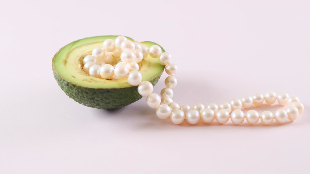 la mitad de un aguacate con perlas en un fondo rosa claro. surrealismo. diseño de alimentos de moda