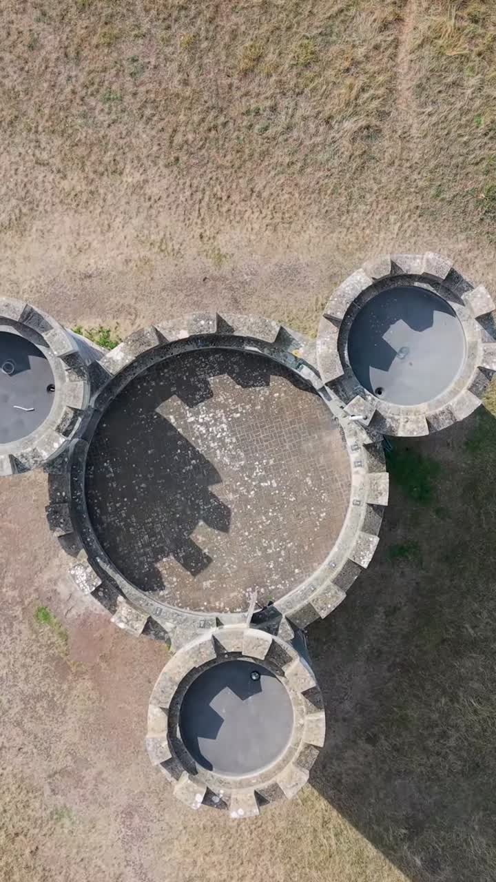 Vertical aerial top-down drone view of Blaise Castle, Bristol, UK. The castle slowly rotates as shadows of its three turrets move clockwise, creating a time-like effect reminiscent of a giant clock