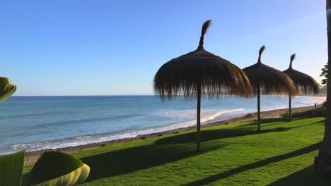tiro de vacaciones de paraíso de ensueño moviéndose a la derecha en marbella malaga vista al mar en costa del sol en españa, plantas tropicales verdes y sombrillas tiki con techo de paja en la playa
