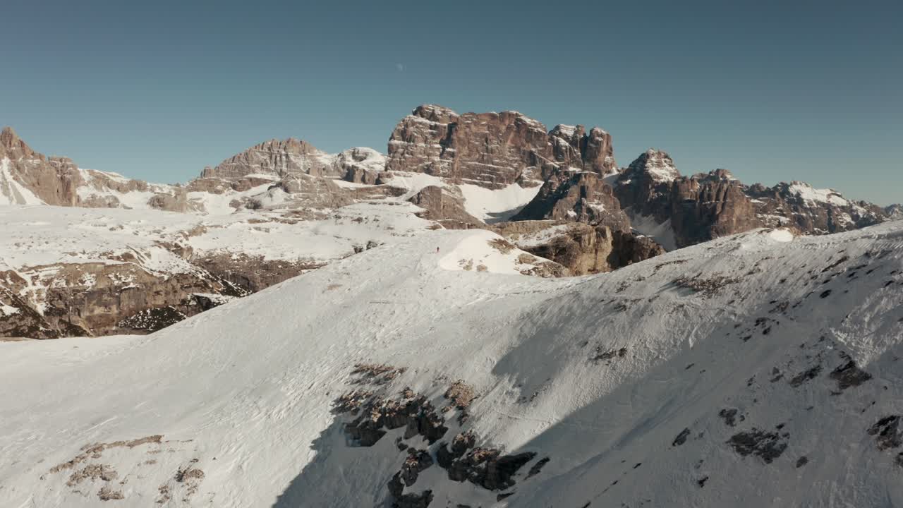 Dolly forward drone shot over hiker walking along a steep snowy ridge