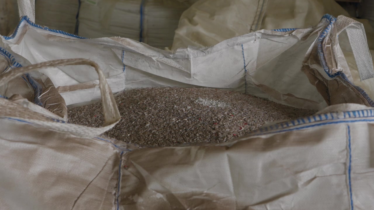 Großer Big Bag gefüllt mit geschredderten recycelten Kunststoffgranulaten in der Fabrik.