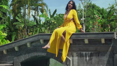 una mujer joven en un vívido vestido amarillo sentada en el puente de un opulento castillo con una piscina en el fondo