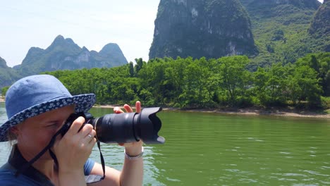 Western-female-tourist-photographing-the-stuning-karst-scenery-on-a-trip-on-the-magnificent-Li-river-from-Guilin-to-Yangshuo,-China