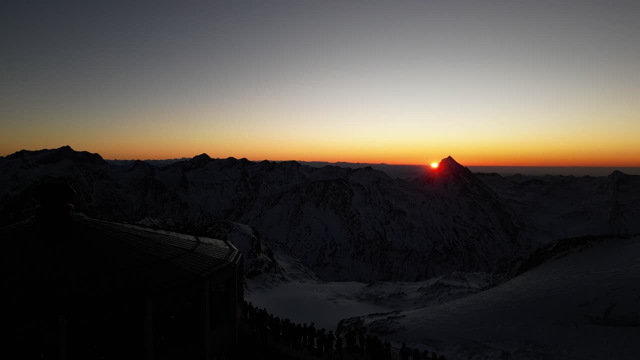 vista aérea: cielo anaranjado, sol en el horizonte, cumbre de los alpes suizos, invierno