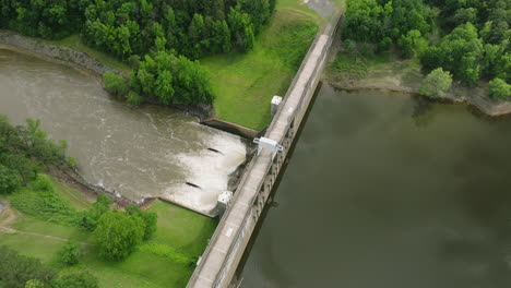 Water-flow-into-Nimrod-Lake-through-concrete-dam,-Aerial-orbit