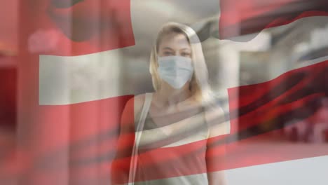 animation of flag of switzerland waving over woman wearing face mask during covid 19 pandemic