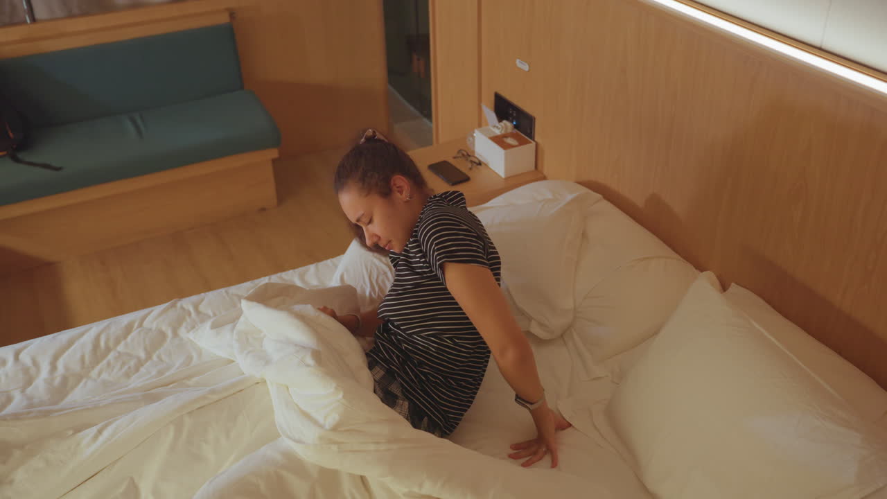 Hotel bed morning woman rising to stretch and prepare, white linens tousled, bedside table with phone and bag, quick breath and rub of eyes, optimistic energy before departure