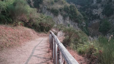 path-outlined-by-brown-fences-in-the-middle-of-nature-in-the-mountains-surrounded-by-trees,-bushes-and-grass-with-a-dry-river-on-a-good-August-day