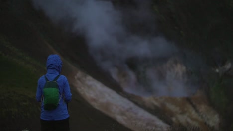 iceland-landscape,-geothermal-hotspring-steam-smoke,-one-person-watching-the-smoke-rising,-camera-tilt-up,-dark-and-moody-evening-atmosphere