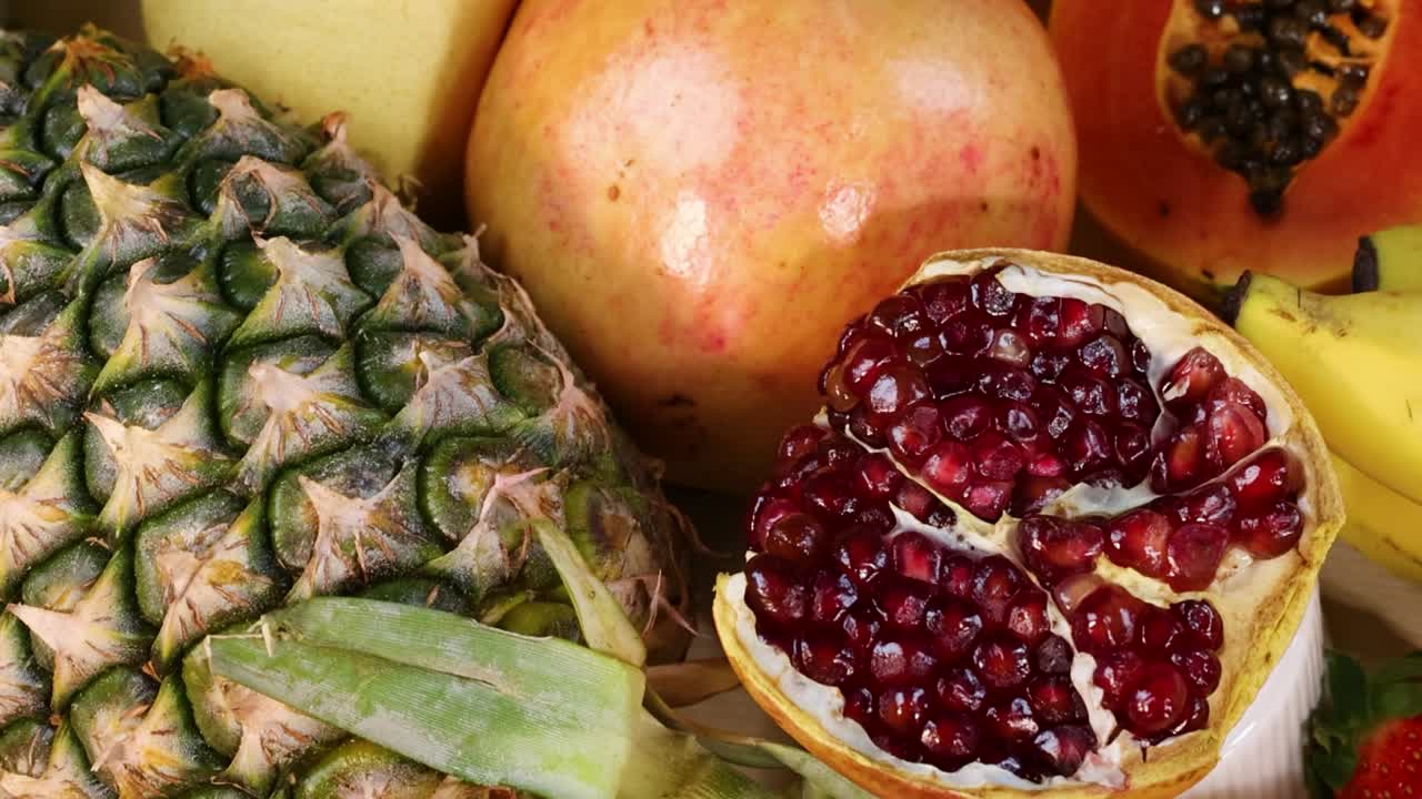 Et levende fugleperspektiv af skiveskårne jordbær, ananas og granatæblekerner på et bord.