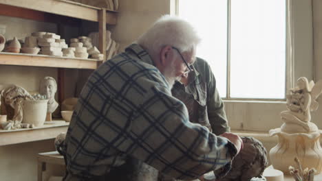 elderly sculptor teaching young woman how to create clay head