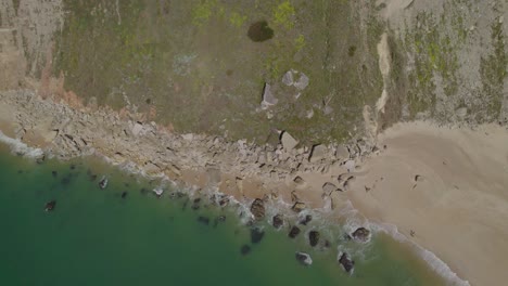 Aerial-top-down-shot-of-the-calm-ocean-waves-crashing-on-the-rocky-coastal-shore-in-Nazare,-Portugal