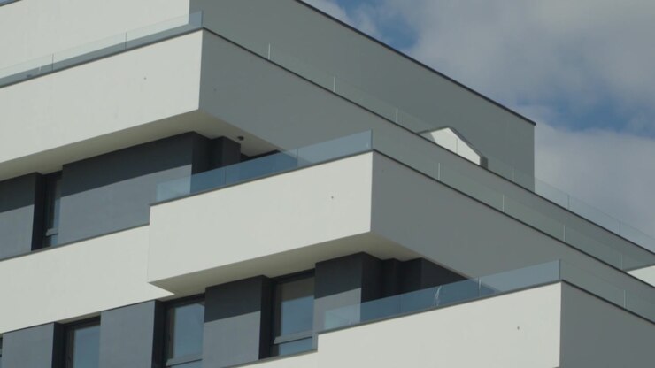 Primo piano dal basso di un moderno edificio residenziale bianco con balconi in vetro contro un cielo nuvoloso.