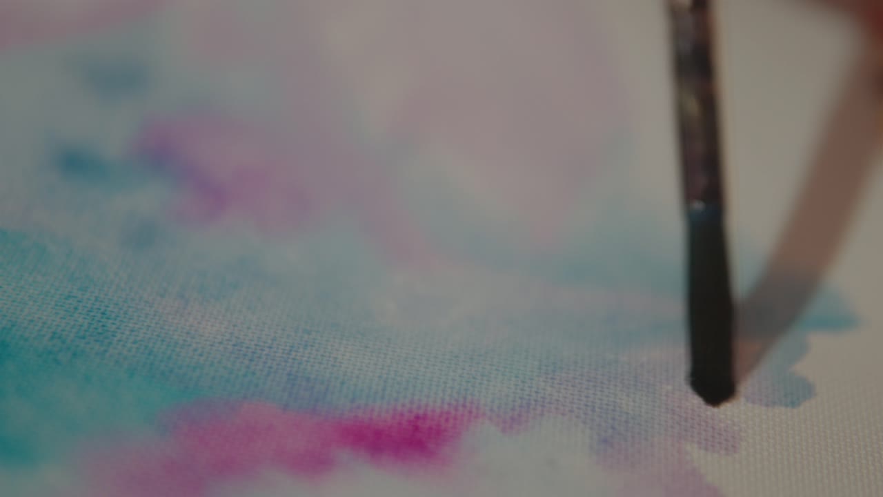 Un primo piano dettagliato di un pennello che sfuma acquerelli vivaci blu, rosa e viola su una tela
