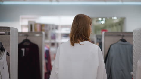 dama caminando en el pasillo de la tienda minorista con estantes de ropa bien dispuestos, mostrando diversos estilos y colores, la atmósfera tranquila y brillantemente iluminada destaca su enfoque mientras explora la moda moderna