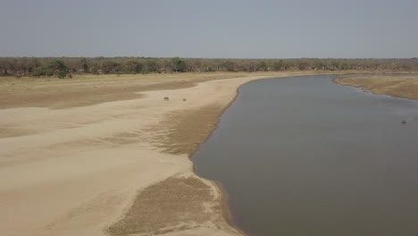 Aerial:-Mother-and-baby-elephant-walk-on-mud-flat-near-African-river