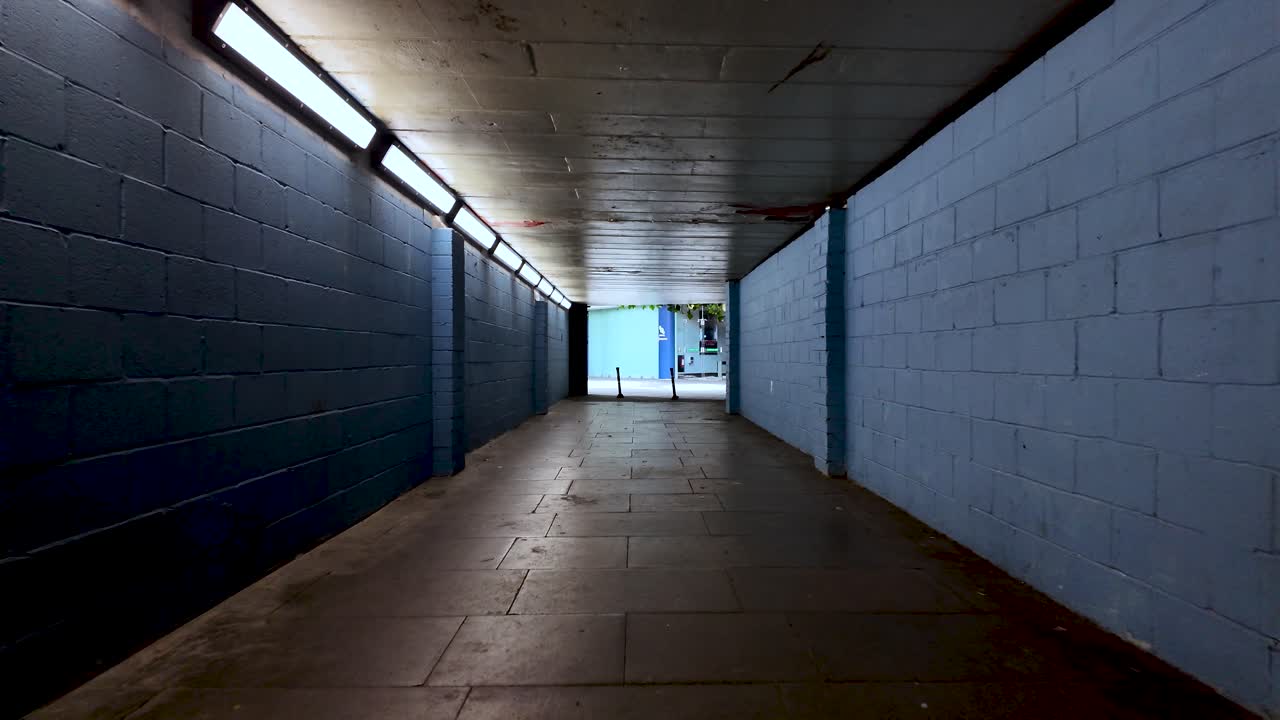 POV of someone walking in a lonely empty underpass with blue brick walls and artificial lights