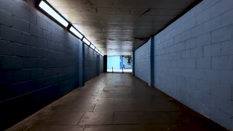 pov of someone walking in a lonely empty underpass with blue brick walls and artificial lights