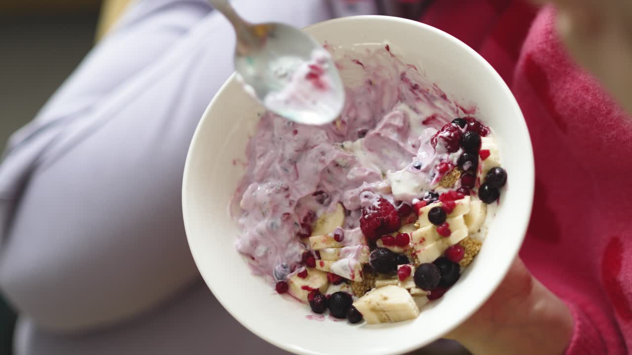 Wanita duduk di sofa menikmati semangkuk sarapan dengan skyr dan buah-buahan hutan, menyoroti gaya hidup sehat, pola makan bergizi, kesehatan pagi hari, dan rutinitas sarapan pagi yang nyaman di rumah.