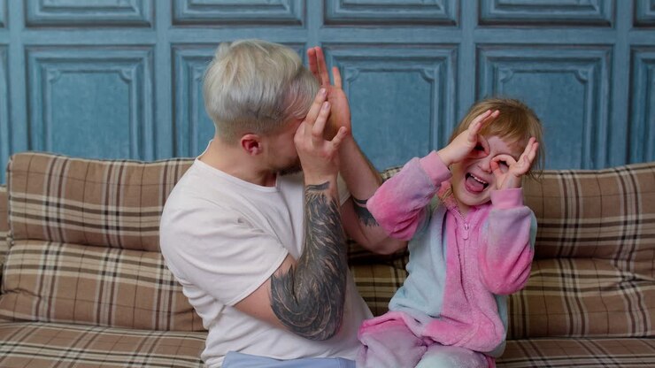 Father and child daughter kid in pajamas fooling sit on couch in living room smile look at camera