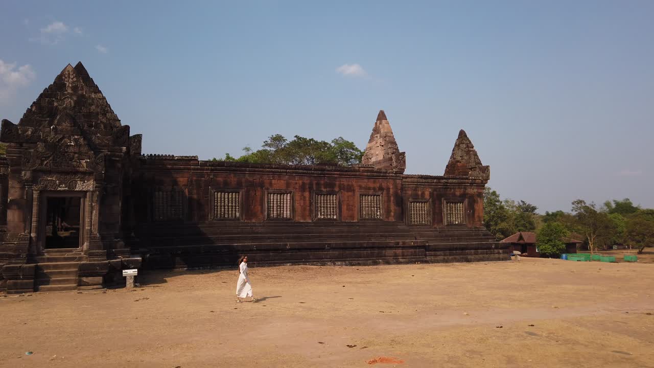 joven hermosa con un largo vestido blanco y gafas de sol caminando cerca del palacio khmer en wat phou complejo de templos hindúes arruinados. champassak, laos, asia. soleado. cultura antigua arquitectura religiosa lenta.