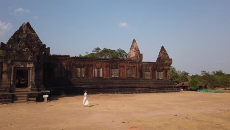 young beautiful woman in long white dress and sunglasses walking near khmer palace in wat phou ruined hindu temple complex. champassak, laos, asia. sunny. ancient culture religious architecture. slow