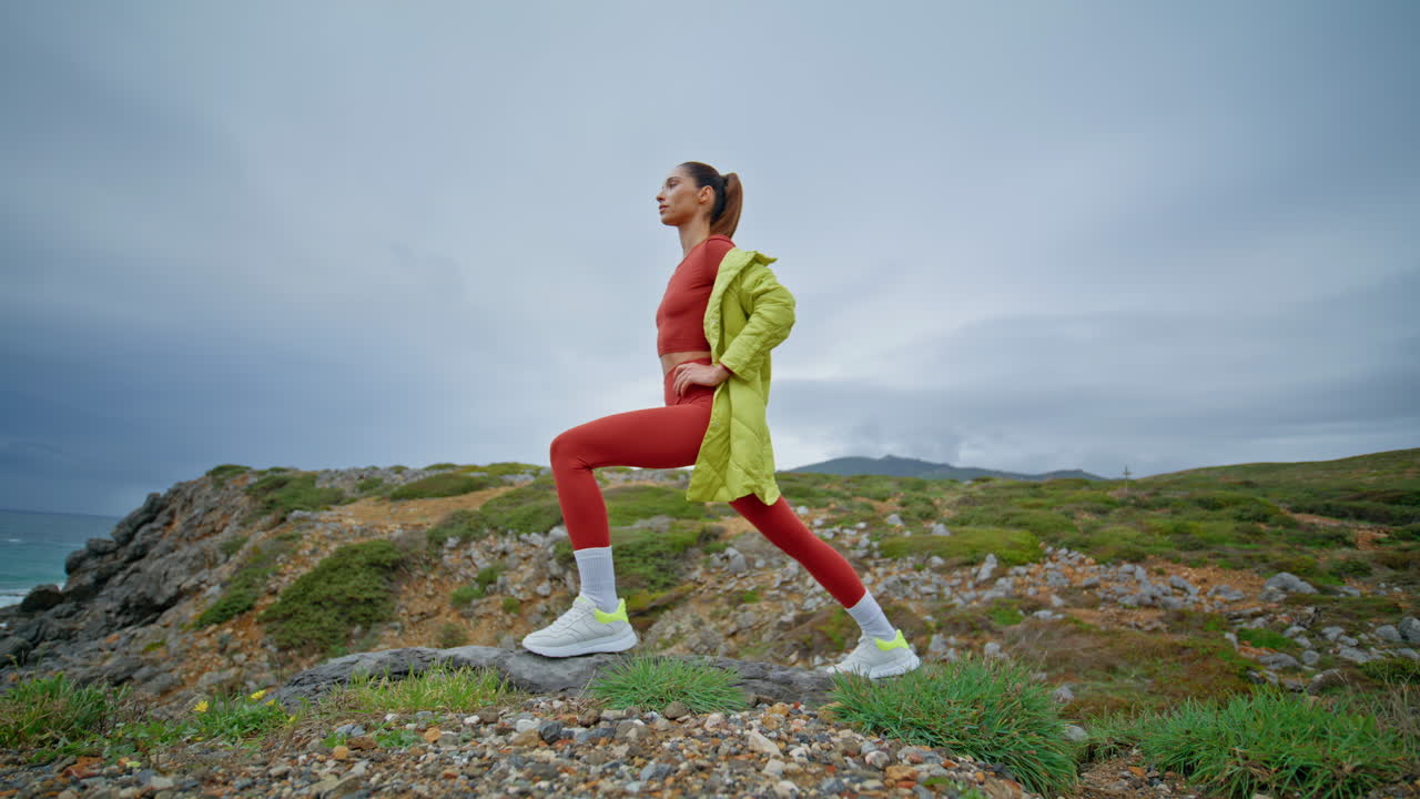 mujer en forma estirando el cuerpo en la costa accidentada. chica deportiva ejercitando naturaleza nublada