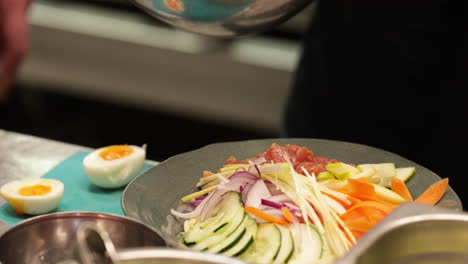 asian salad - chef putting fresh cut tuna meat on the side of vegetable salad