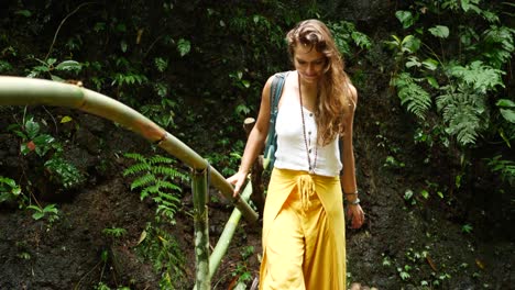 una joven mujer atractiva camina sobre un pequeño puente de bambú sobre un pequeño arroyo de agua siendo feliz con una sonrisa en una hermosa y exuberante jungla en bali