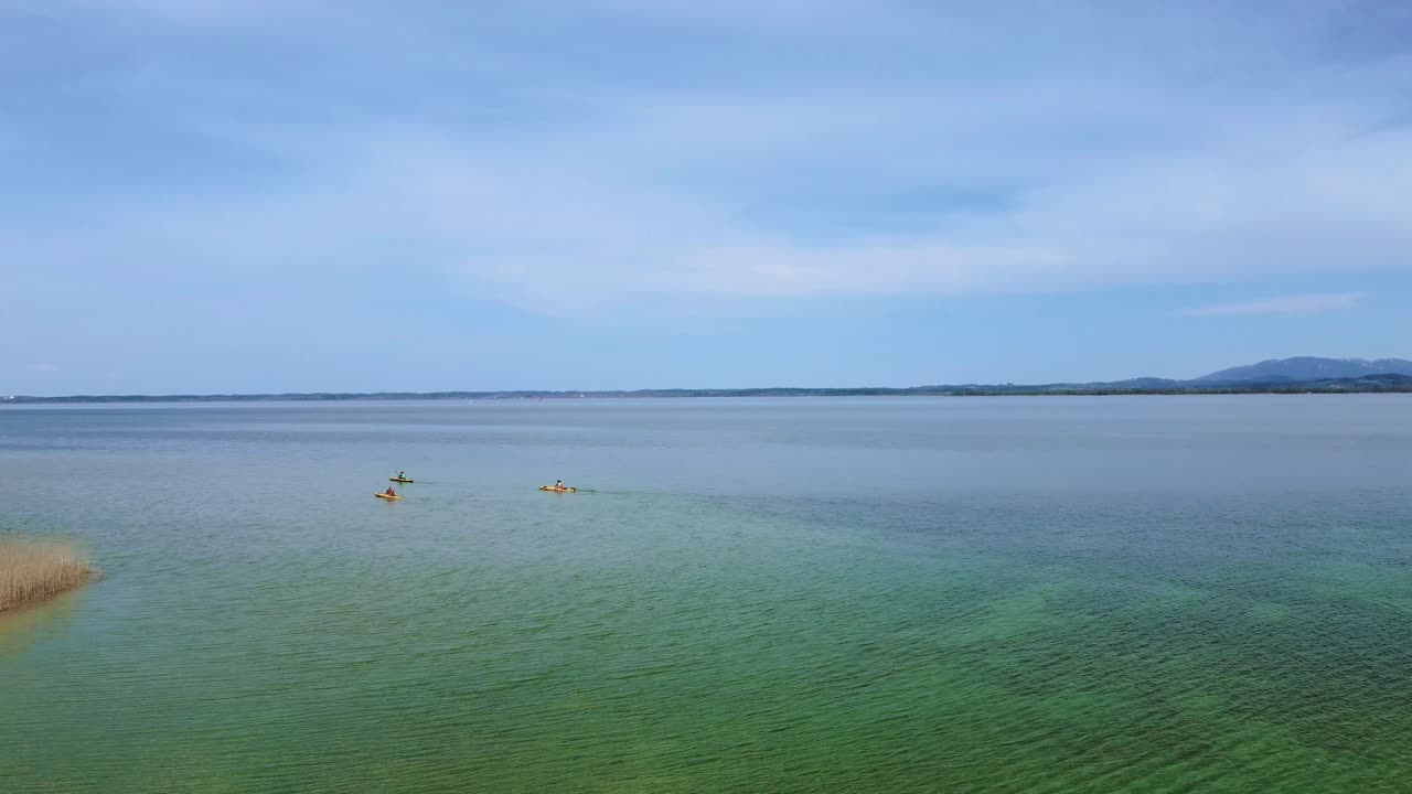 화창한 날 배경에 아름다운 하늘, 맑고 푸른 물, 알프스 산맥이 있는 시골 시골에 있는 바이에른의 유명한 호수 키엠제에서 카약 보트 위의 경치 좋은 4k 비행