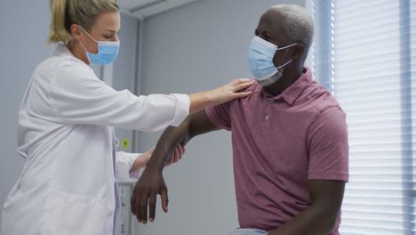 Médico-Ortopédico-Femenino-Diverso-Que-Examina-A-Un-Paciente-Masculino-Con-Máscaras-Faciales