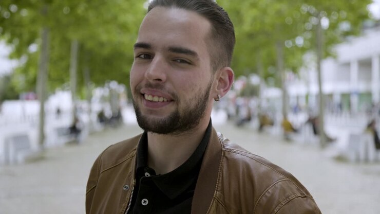 Ragazzo barbuto elegante e sorridente con piercing che guarda in macchina