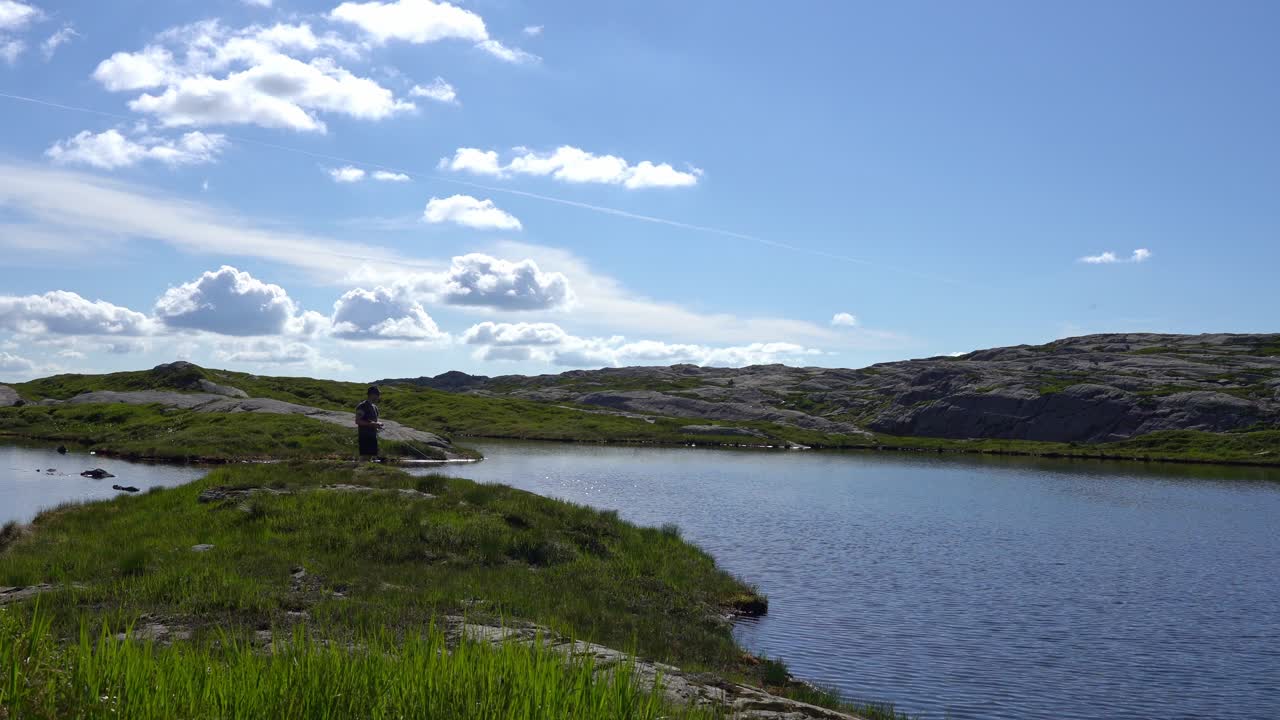 hombre pescando desde la orilla de la hierba del pintoresco lago de montaña en un día soleado
