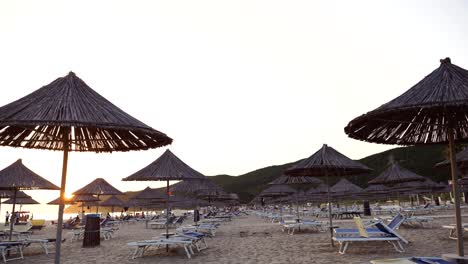 Albanian-empty-beach-at-sunset,-straw-umbrellas,-and-sunbeds