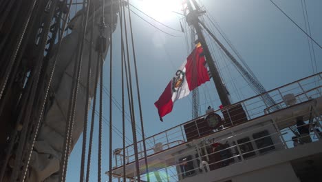 El-Estilo-Del-Sol-Brilla-A-Través-De-Las-Cuerdas-De-Los-Barcos-Altos-Y-Los-Aparejos-Mientras-Una-Gran-Bandera-Colorida-Ondea-En-La-Brisa