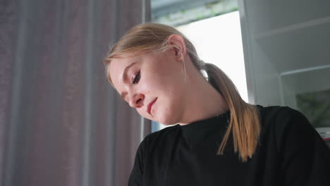 close up of young female massage therapist smiling softly while focused on work, side view with curtain and cabinet in background, soft natural light illuminating her calm and professional expression