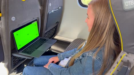 woman working on laptop with green screen on a train