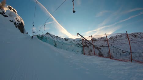 Mit-Einem-Skilift-Einen-Hügel-Hinauf,-Entlang-Eines-Sicherheitsnetzes-Und-Die-Sonne-Direkt-Hinter-Dem-Horizont