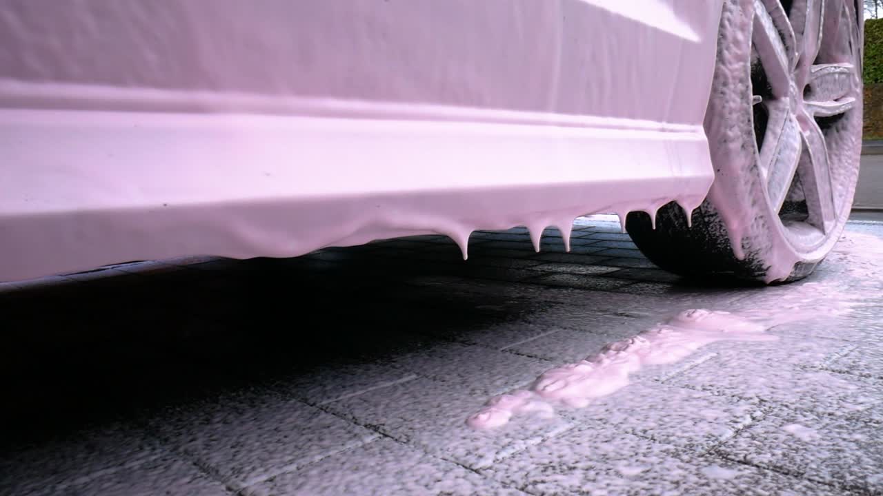 Side Skirt of a Black Car With Dripping Pink Snow Foam