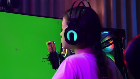 close up back view of asian girl streamer screaming goal and dancing celebrating winning game on green screen computer.  live stream video game, desk illuminated by rgb led strip light