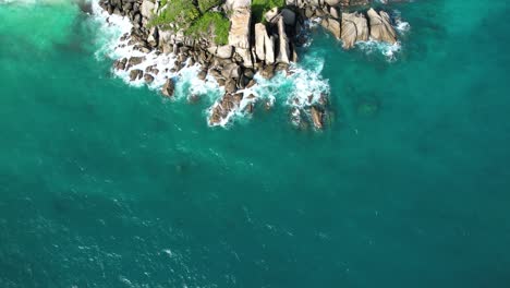 Bird-eye-drone-shot-of-north-east-point-beach,-huge-rock-boulders-waves-crushing-on-and-turquoise-water,-Mahe-Seychelles-30fps